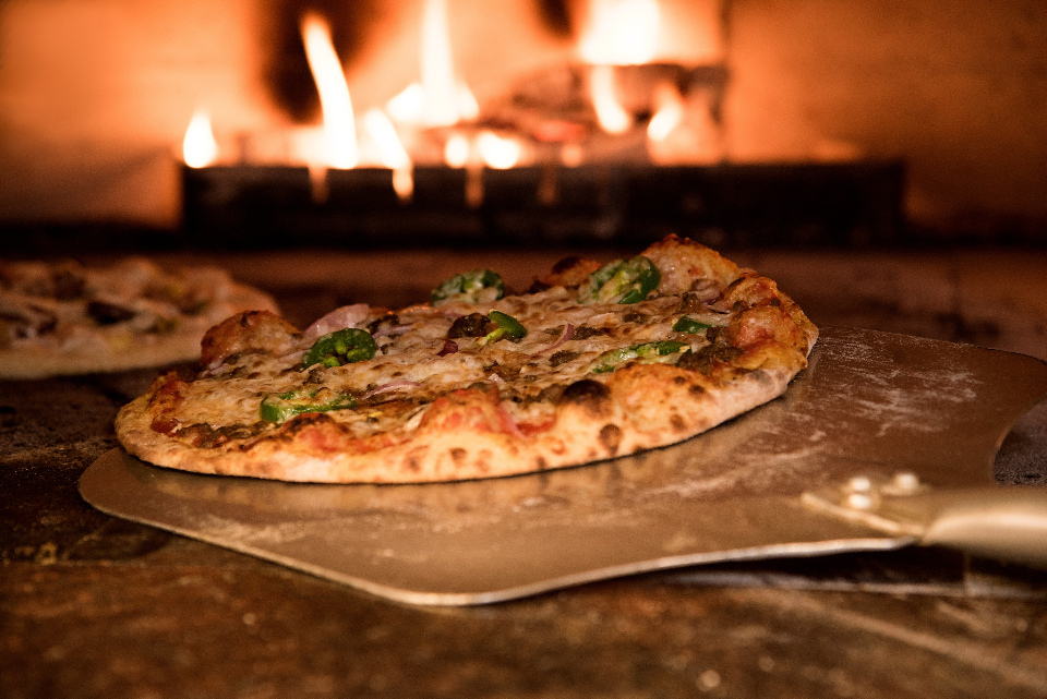 Pizza appena sfornata su una pala, davanti al forno acceso